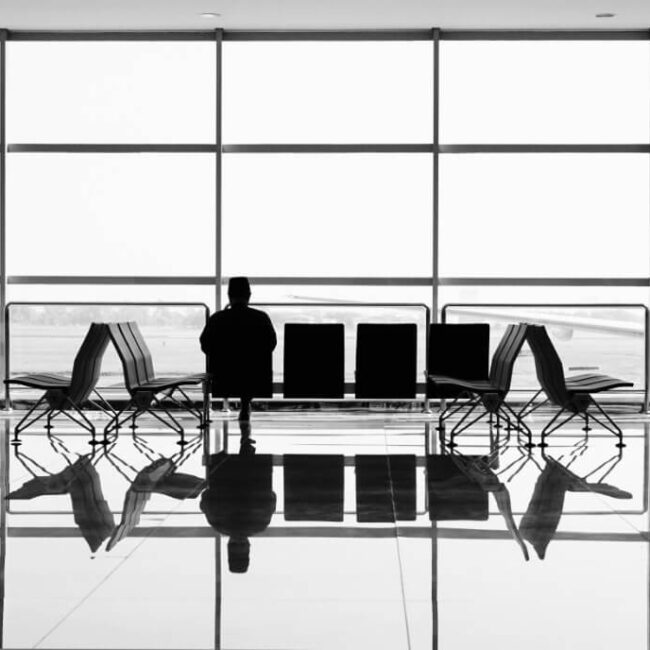 Silhouette of a person sitting alone in an airport terminal with luggage nearby