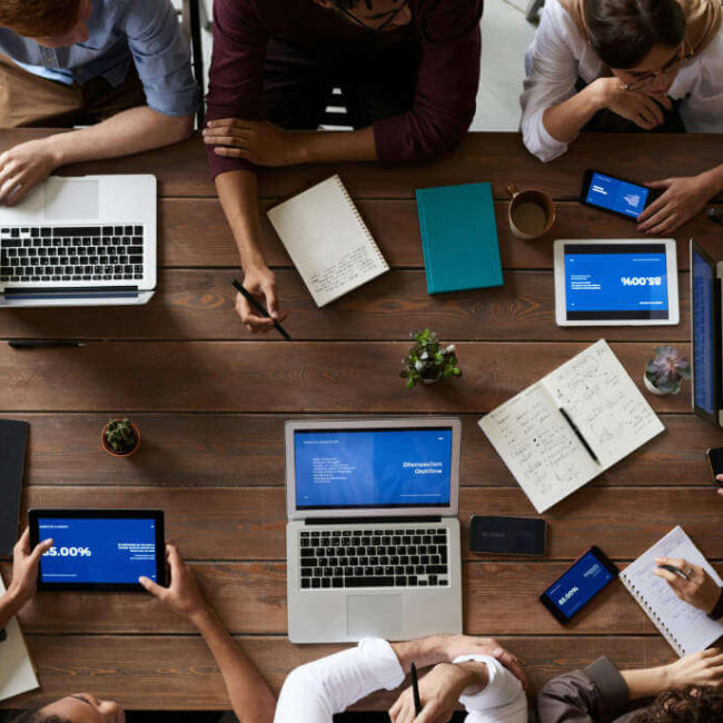 Top view of a diverse group of professionals working together at a large table with laptops and tablets