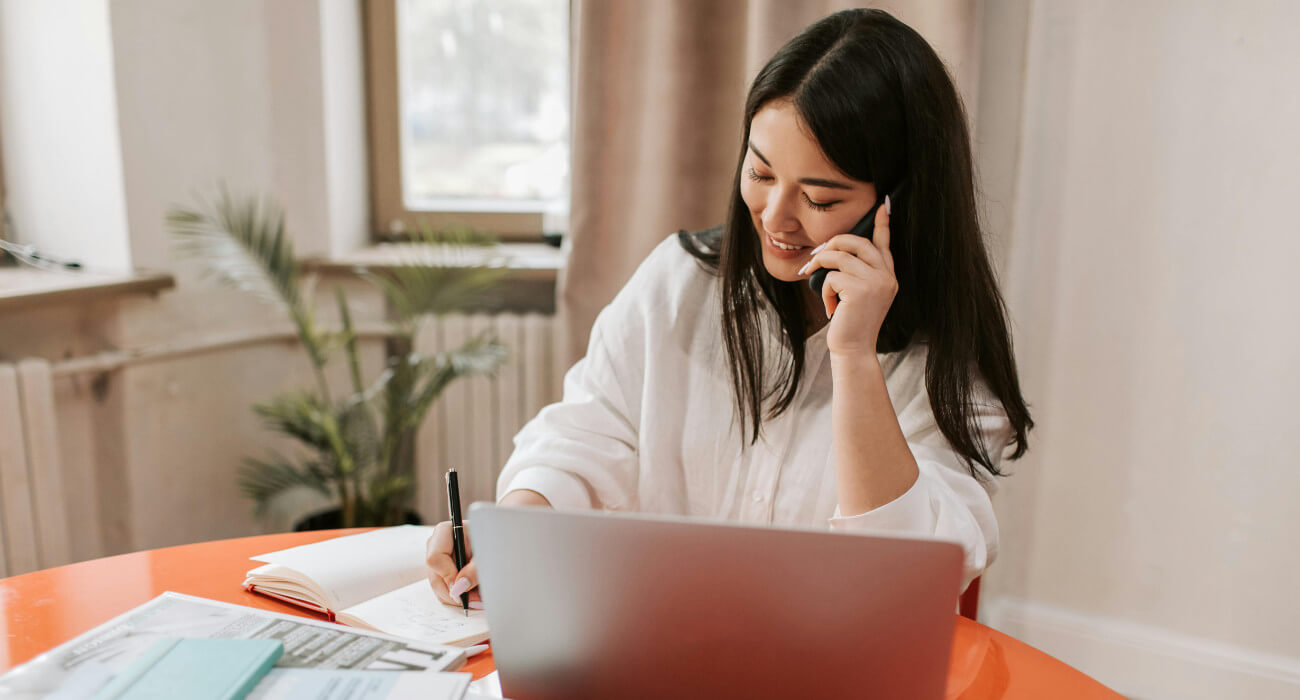 A woman taking a call sitting at a desk on her laptop